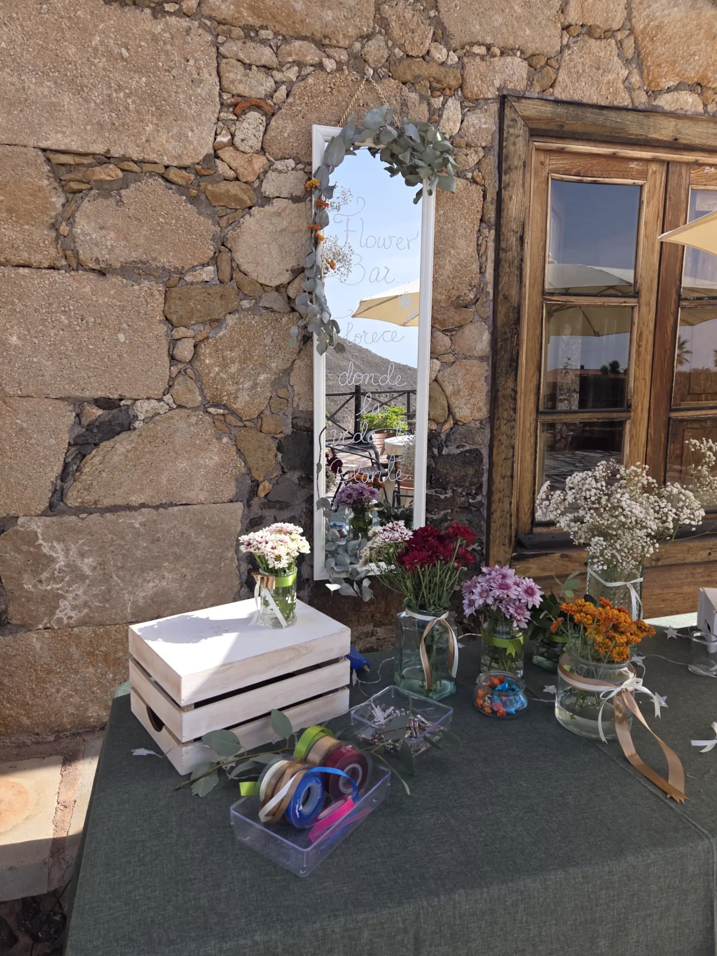 Mesa del flower bar con botes de crisantemos, paniculata y eucalipto junto a un espejo decorado